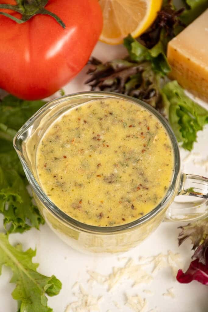 A serving glass filled with homemade Italian Dressing surrounded by lettuce.
