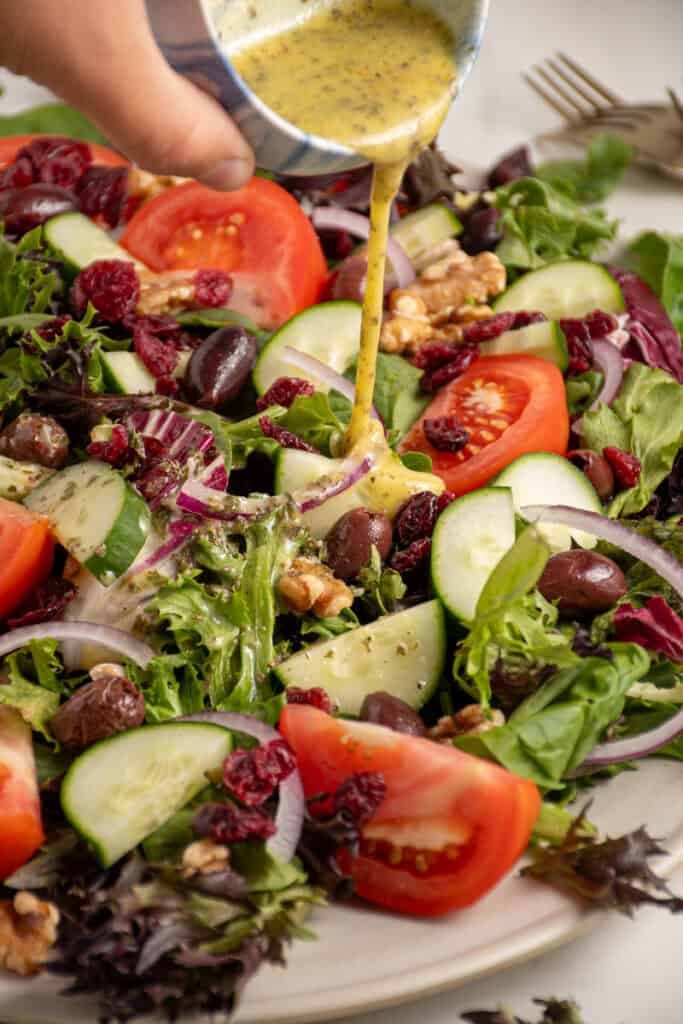 A large platter full of spring mix salad with tomatoes, cucumbers, red onion, walnuts, dried cranberries, and olives.