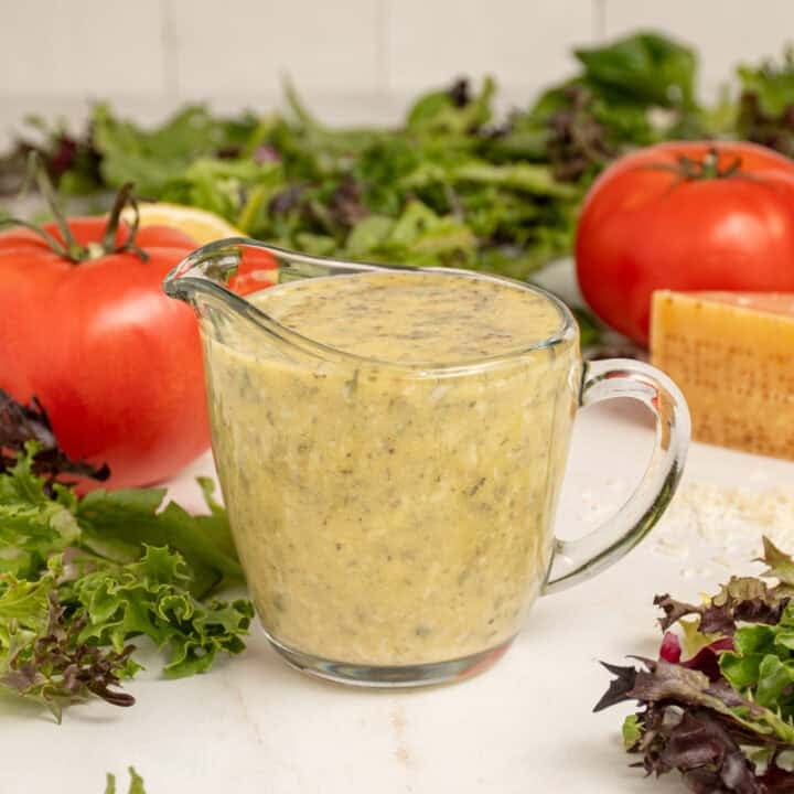 A serving glass filled with homemade Italian Dressing surrounded by lettuce.