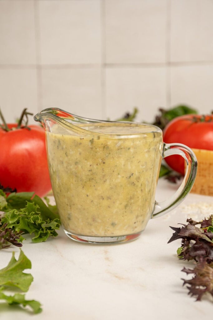 A serving glass filled with homemade Italian Dressing surrounded by lettuce.