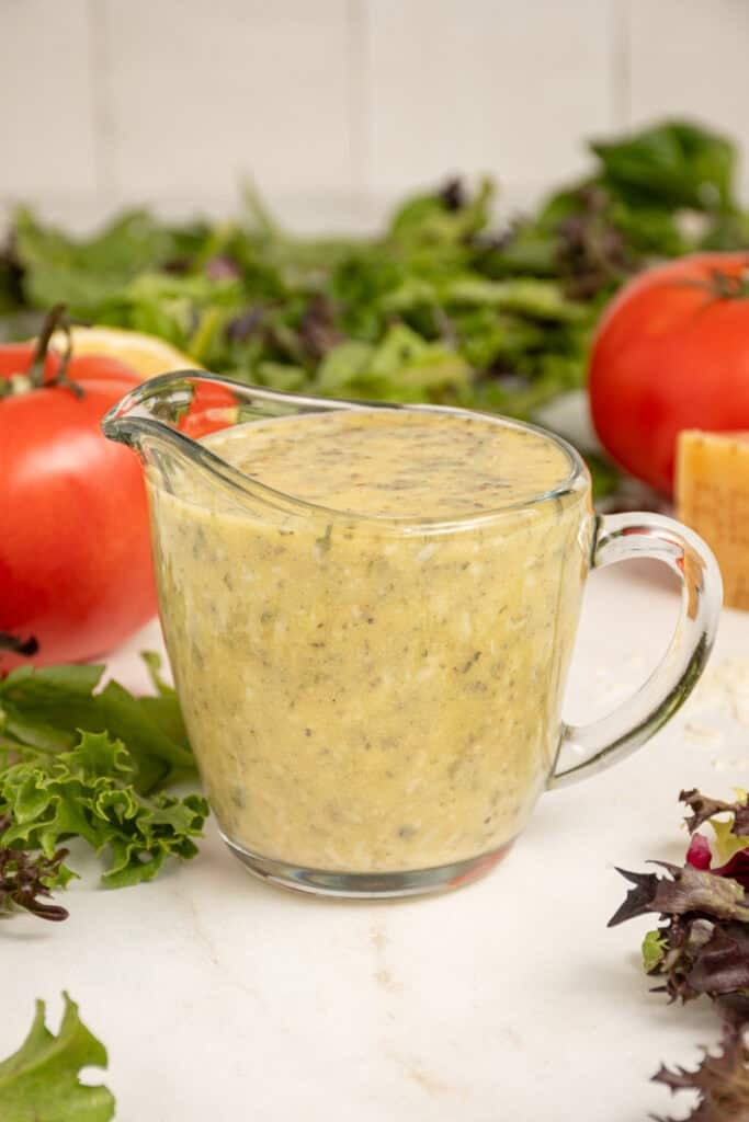 A serving glass filled with homemade Italian Dressing surrounded by lettuce.