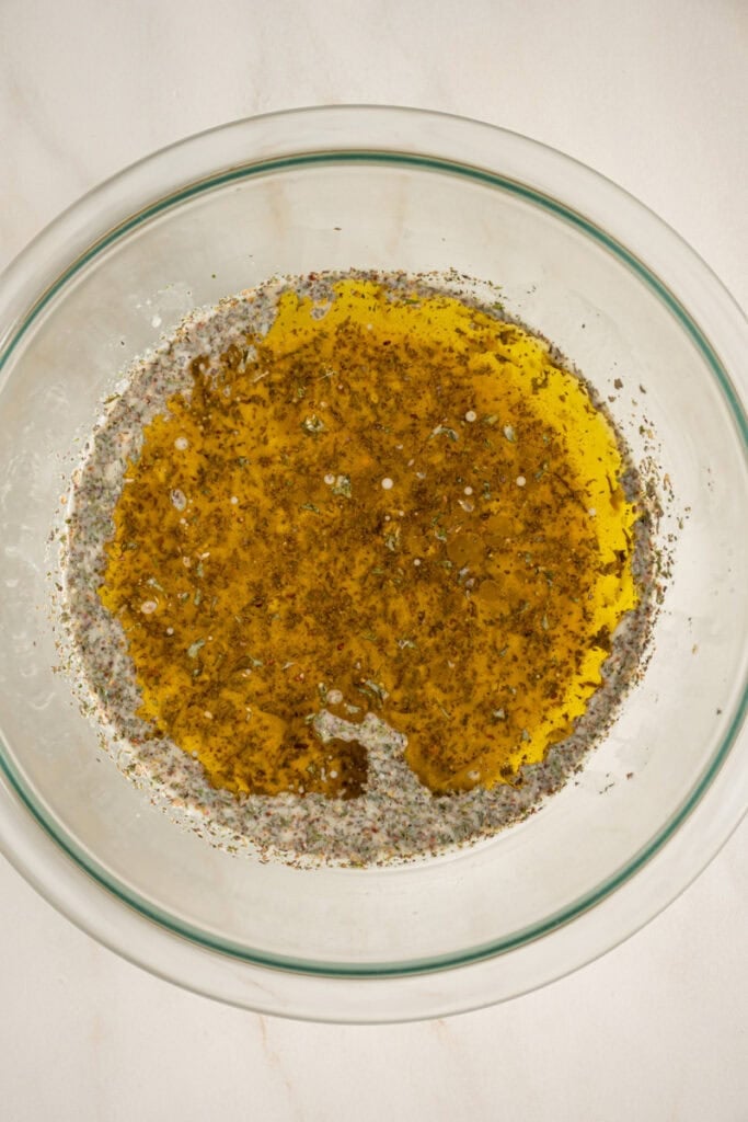 Adding the olive oil to the bowl to make italian dressing.