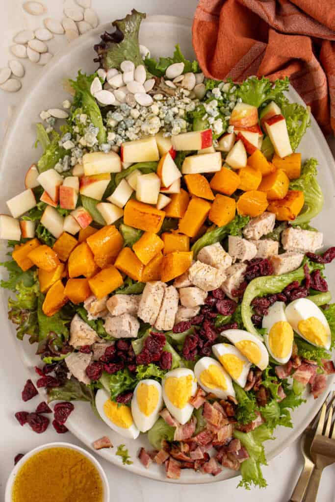 A platter with Fall Cobb Salad with butternut squash, roast chicken, dried cranberries, and pumpkin seeds.