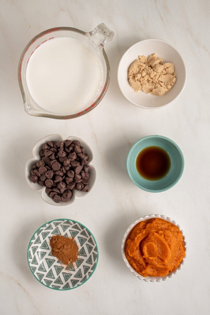 Ingredients for making pumpkin spice hot chocolate laid out on a table top.