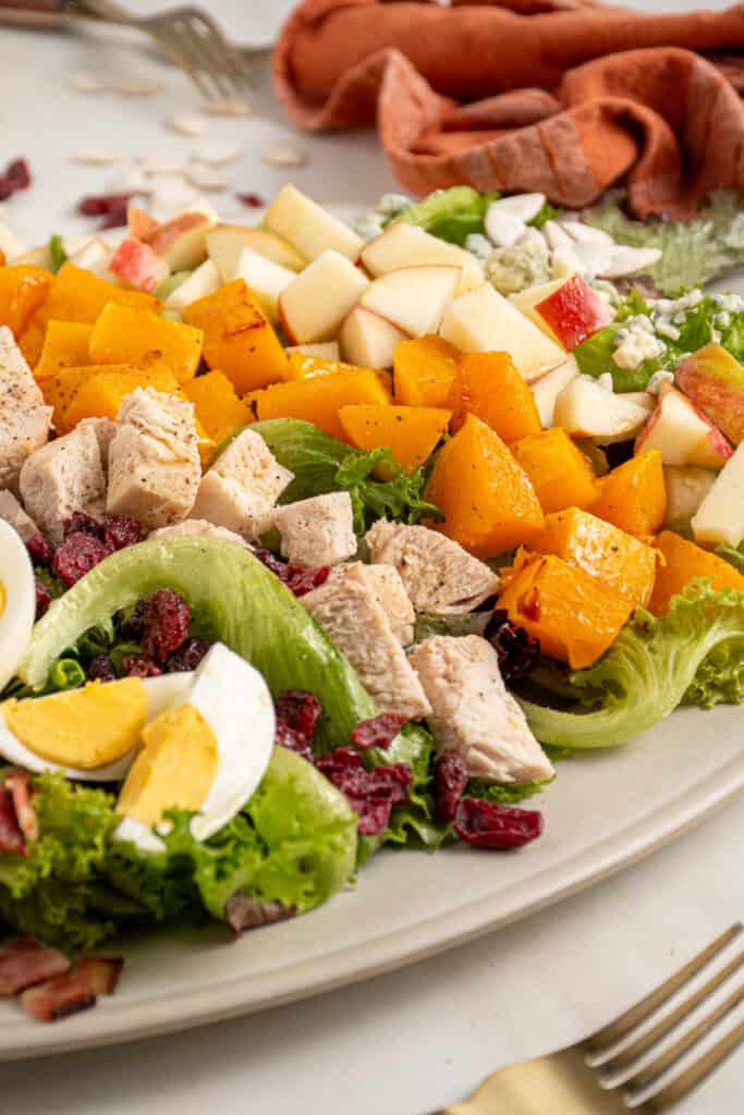 A platter with Fall Cobb Salad with butternut squash, roast chicken, dried cranberries, and pumpkin seeds.