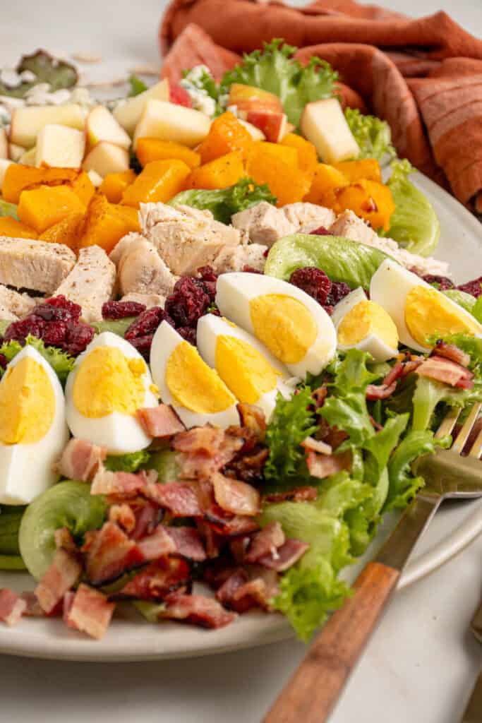 A platter with Fall Cobb Salad with butternut squash, roast chicken, dried cranberries, pumpkin seeds, and hard boiled eggs.